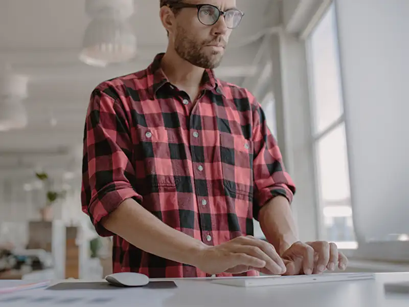Man wearing plaid shirt tying at a computer.